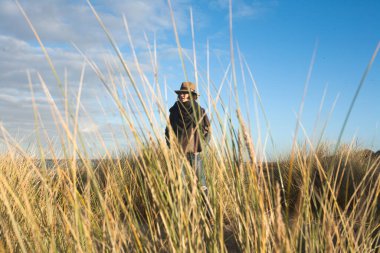 Güzel bir genç kadın, Belçika sahillerinde büyüyen kum çimlerinin arkasında dururken. Moda mankeni gözlerini kaçırıyor ve sonbaharda şapkalı bir taşra derisi elbise giyiyor.. 