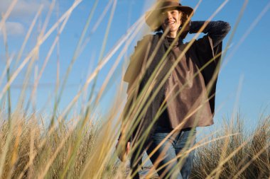 Güzel, zarif bir kadın, kameraya gülümserken. Manken Belçika sahillerinde büyüyen kum çimleri arasında fotoğraflandı. Kışın kırsal alanda çekim..