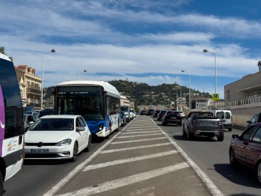Cannes, France-02.09.2025 otobüsleri ve arabaları, binalar ve açık mavi gökyüzünün altındaki uzak bir yamaç tarafından çerçevelenmiş hareketli bir caddeyi işgal ediyor..