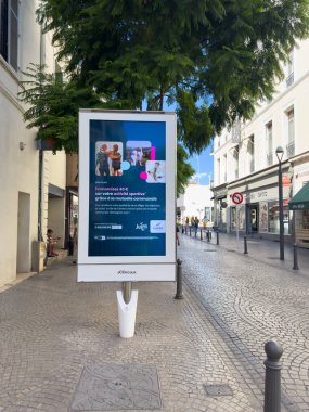Cannes, Fransa-02.09.2025 Hareketli bir şehir caddesinde belirgin bir dinamik reklam duruyor, yaklaşan yerel olayları gözler önüne seriyor ve açık mavi bir gökyüzü altında toplumsal çatışmaları davet ediyor..