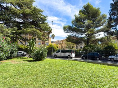 Cannes, Fransa-02.09.2025 güneşli bir günde yeşil bir parkta, uzun ağaçlar gölgelik ve klasik binalar arka planda durarak huzurlu bir şehir kaçışı yaratıyor..