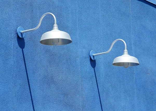 Blue stucco wall with light fixtures and shadows in daytime