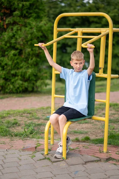 Odaklanmış genç çocuk dışarıda spor aletlerini kullanarak güç topluyor ve sıcak bir yaz gününde parkta formda kalıyor.
