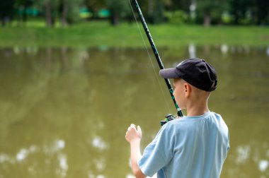 Gölün kenarında balık tutan genç bir çocuk. Tasasız çocukluk kavramı ve doğadaki farkındalık.
