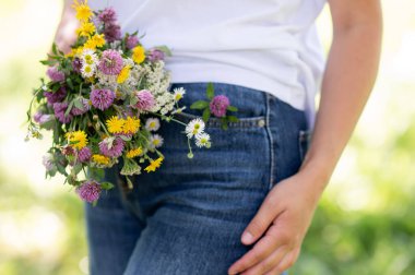 Mavi kot pantolon giyen, elinde kır çiçekleri, doğa konsepti, günlük yaşam tarzı, yaz tatili ve çiçeklerle gezen bir kadın.