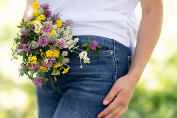 Mavi kot pantolon giyen, elinde kır çiçekleri, doğa konsepti, günlük yaşam tarzı, yaz tatili ve çiçeklerle gezen bir kadın.