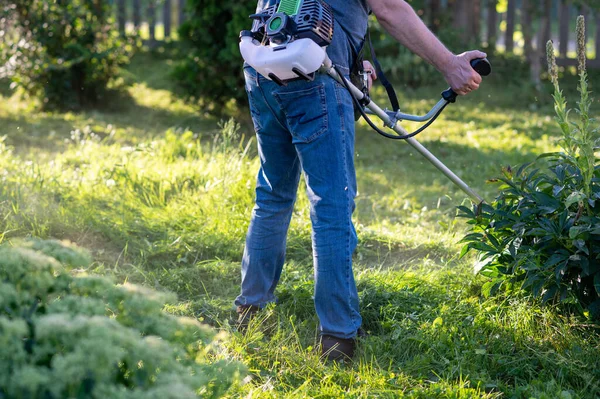 Arka bahçede çim biçme makinesiyle uzun otları kesen kot giyen adam mevsimlik çim bakımı ve bahçe işleri kavramı.