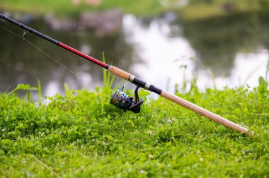 Dönen bobinli olta taze yeşil çimenlerin üzerinde duruyor, açık hava gezisi sırasında ya da arazide olta takımlarını yakından görüyor.