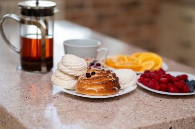 Konforlu mutfak sahnesi çaydanlık, marşmelov, taze çörekler ve meyveler tezgahın üstünde, sıcak ev havası.