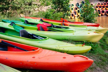 Nehir kıyısında çok renkli kanolar dizildi, yaz rafting macerasına hazırlar, açık hava, doğa, su sporu, güneşli bir gün.