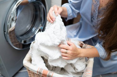 Çamaşır sepetinden kirli çamaşırları çıkaran ve çamaşır makinesine koymaya hazırlanan kadın. Ev işleri ve ev temizliği kavramı.