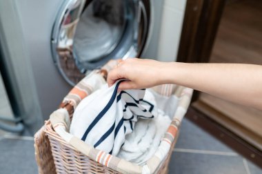 Çamaşır sepetinden çamaşır çıkaran kadın el çamaşır makinesine çamaşır koymaya hazırlanıyor. Ev işleri ve temizlik kavramı.