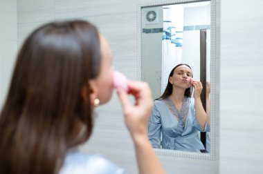 Aynanın önünde süngerle makyaj yapan kadın, güzellik konsepti ve kişisel bakım.