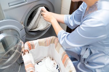 Kirli çamaşırları çamaşır makinesine yükleyen kadın, çamaşır yıkamaya hazırlanan ev işleri ve ev temizliği kavramı.