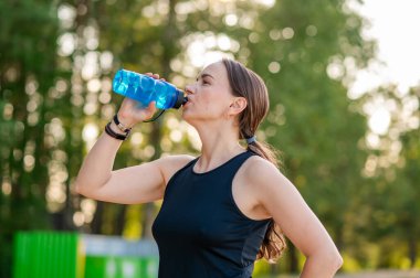 Formalı spor kıyafetleri içinde güzel bir kadın ormanda koşmaya ara veriyor, temiz havanın tadını çıkarıyor ve açık havada sağlıklı yaşam tarzını geliştiriyor.