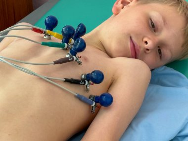 ECG prosedürü sırasında göğüs ve kol elektrotlarıyla kalp sağlığı kontrolü için kanepede yatan çocuk.