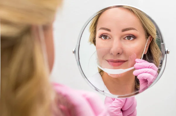 master of permanent make-up in a mask on his face looks in the mirror