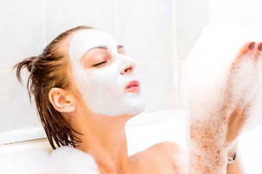 Yüzünde maske olan kadın banyoda yalan ve köpük onun avucunda üfleme