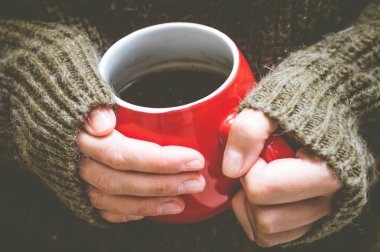 Kırmızı fincan bir Yün kazaklı bir kadın elinde kahvesiyle