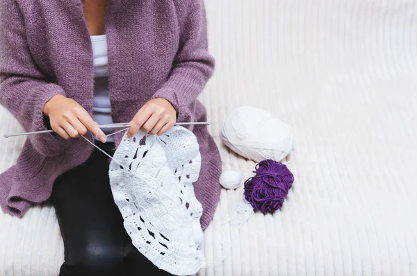 Girl knits with her knitting needles sitting on the couch. Concept hobby