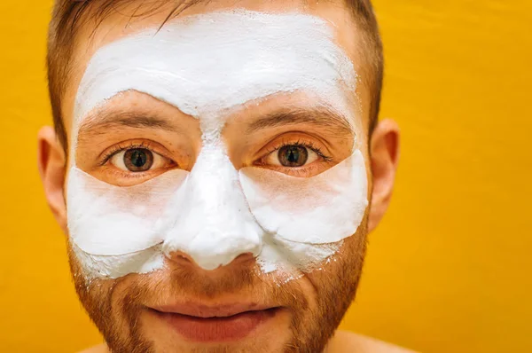 Young man with facial mask on a yellow background. Concept care for yourself for men. Close-up portrait.
