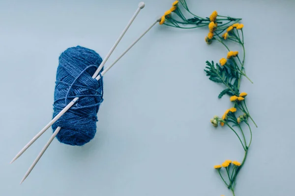 Tangle of woolen threads with knitting needles on a blue background. Yellow flowers on my side. Concept Handicrafts