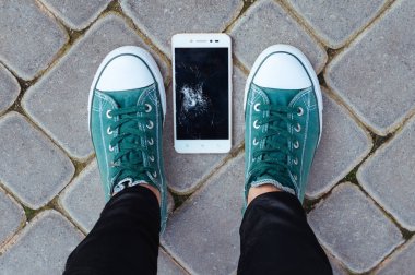 Bozuk bir ekranı olan akıllı telefon asfalttaki kişinin ayaklarında yatıyor.