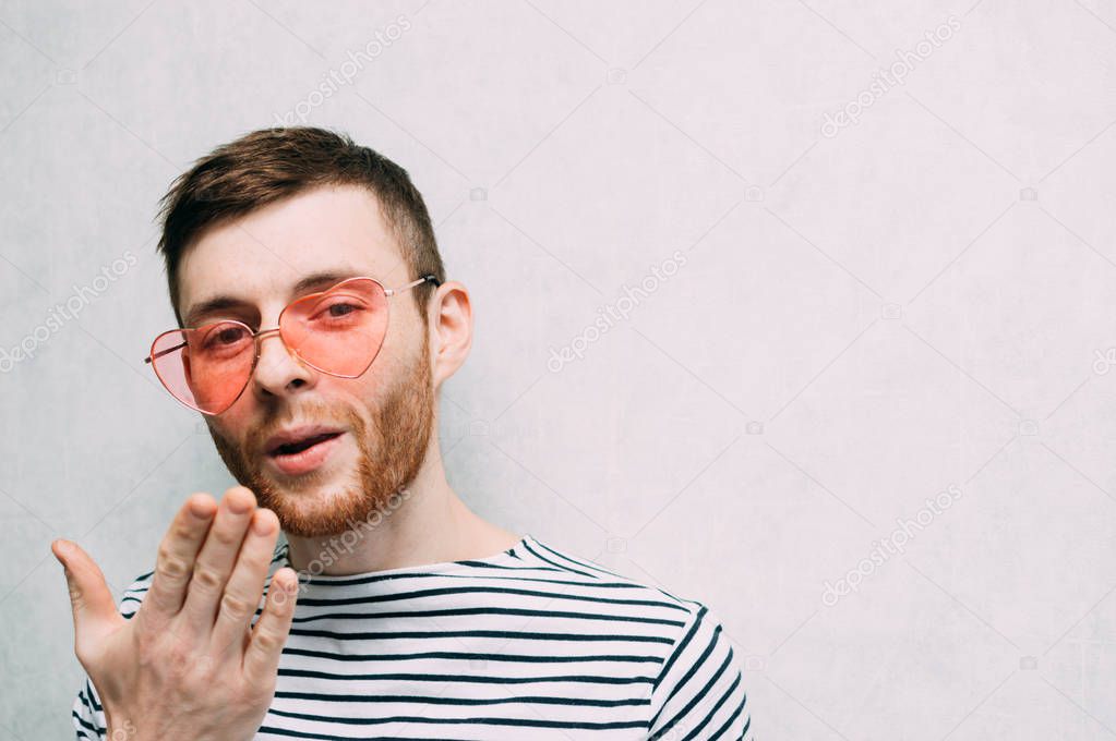 Young man in pink glasses sends a kiss. Valentine's day holiday. Light background.