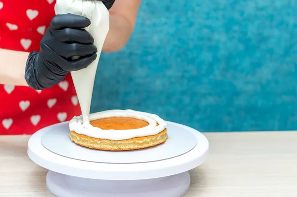 Confitero aplica la crema en el pastel de bizcocho. Proceso de elaboración de pasteles. Copiar espacio — Foto de Stock