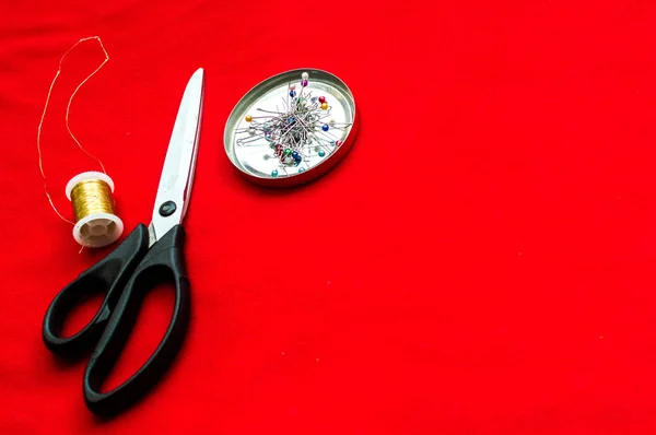 Tesoura para cortar, agulhas e fios em um pano vermelho. Roupas de design de conceito . — Fotografia de Stock
