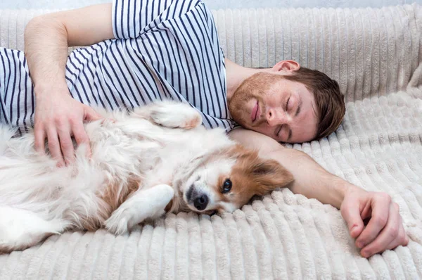 ベッドの上で抱き合って犬と一緒に寝ている若い男の肖像画 — ストック写真