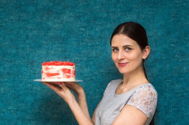 Ev hanımı elinde mavi bir arka plan üzerinde beyaz ve mercan renkli sünger kek tutar. Kopyalama alanı