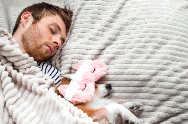 Perro rojo duerme en una máscara de dormir rosa con su dueño en la cama. Concepto fin de semana y descanso — Foto de Stock