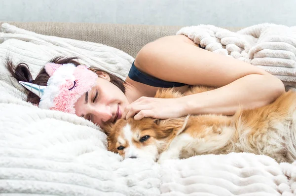 Портрет молодої жінки з маскою для сну та піжамою, що обіймає свого собаку. Концепція відпочинку і сну . — стокове фото