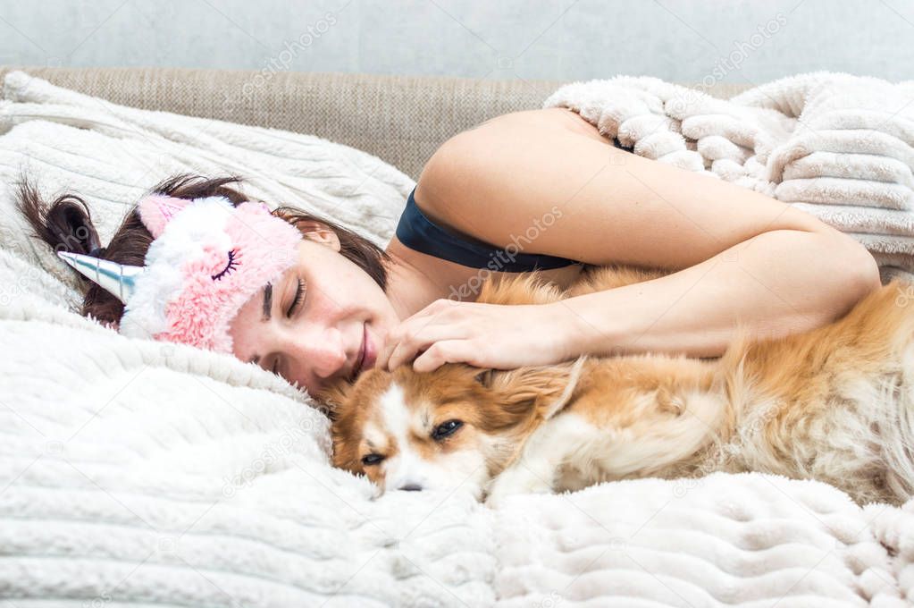 Portrait of a young woman with a sleep mask and pajamas hugging her dog. Concept of rest and sleep.