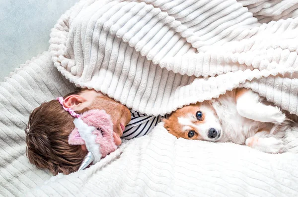 Молодий чоловік спить в рожевій масці для сну в ліжку під килимком зі своїм собакою в обіймах — стокове фото