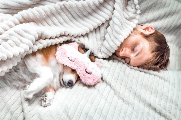 Червоний собака спить в рожевій спальній масці зі своїм власником у ліжку. Концепція вихідних і канікул — стокове фото