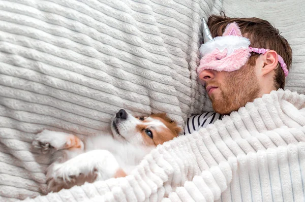 Крупним планом портрет молодого чоловіка в рожевій масці спить у ліжку під килимком зі своїм собакою — стокове фото
