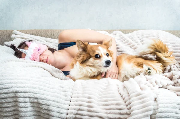 Портрет молодой женщины в маске для сна и спальной пижаме в постели. Рядом красная собака. — стоковое фото