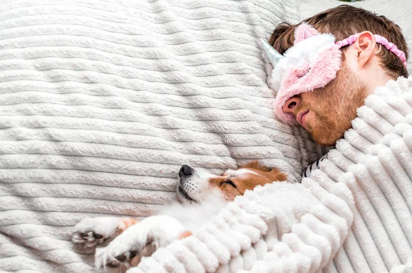 Retrato de cerca de un joven con una máscara rosa durmiendo en una cama debajo de una alfombra con su perro. Copiar espacio — Foto de Stock