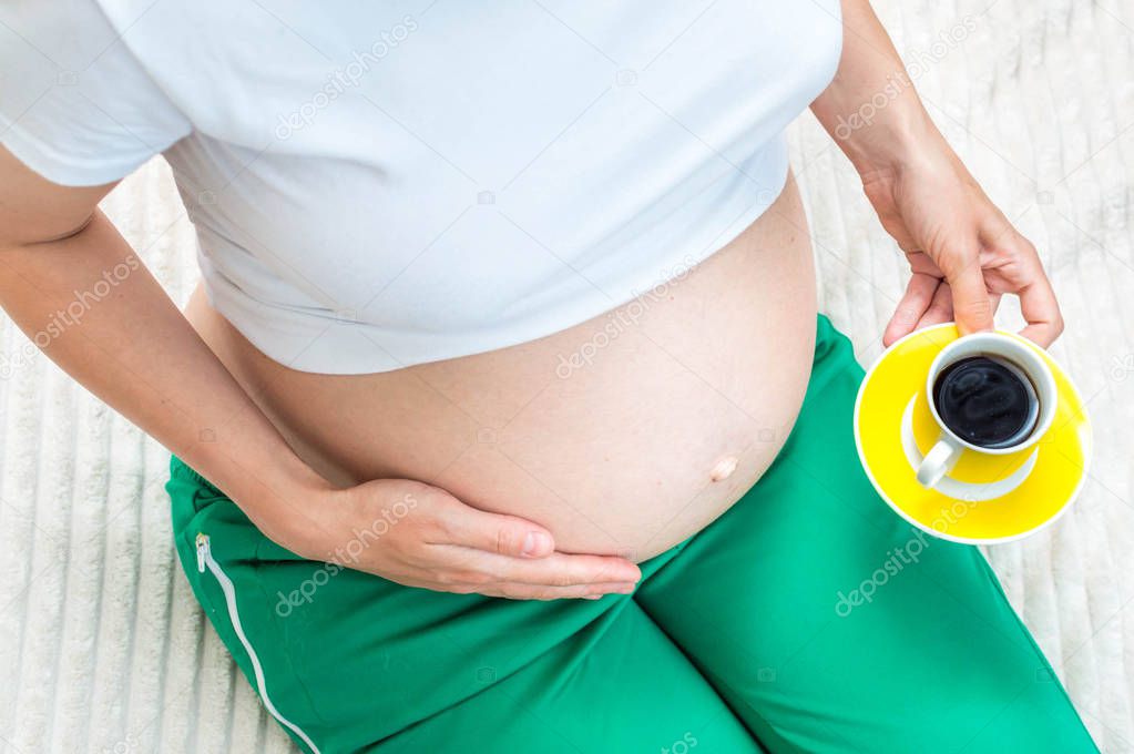 pregnant woman holds in her hand a cup of coffee. Close-up. Caffeine concept during pregnancy