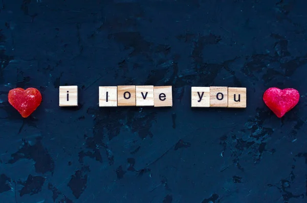 Inscripción en letras de madera Te amo sobre un fondo negro y dos corazones rojos. Romance. Concepto de confesión de amor. Día de San Valentín — Foto de Stock