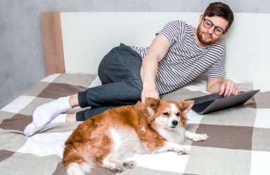 Evde dizüstü bilgisayarda çalışan genç bir adam ve yanında da bir köpek. Uzaktan Çalışan Kavram