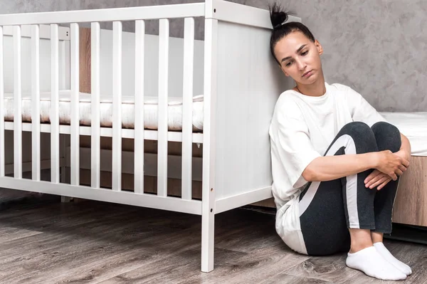 young woman sits sad by the crib. Postpartum Depression Concept