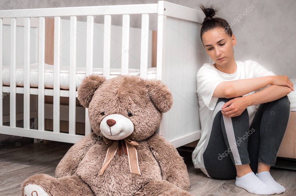 young woman sits sad by the crib. Postpartum Depression Concept