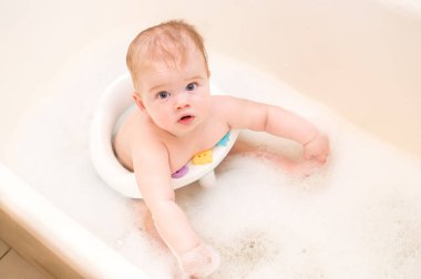 Bebek, banyoda yıkanmak için çocuk sandalyesinde banyo yapıyor. Portre. Banyo köpüğü.