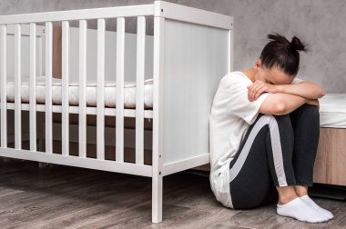 young woman sits sad by the crib. Postpartum Depression Concept clipart