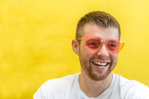 Young man in pink sunglasses on a yellow background. Happiness concept, gender
