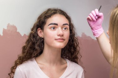 Kaş ustası, kaş kalemi olan genç bir kadının kaşlarının şeklini çizer. Güzellik salonunda kınalı kaş boyama prosedürü