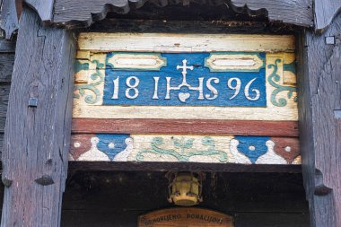 Yeşil tarlalar ve çiçek açan doğa, dinginlik ve miras cazibesi ile çevrili, sakin bir gökyüzünün altında kırmızı kiremitli bir çatı içeren tuhaf tarihi ahşap şapel..